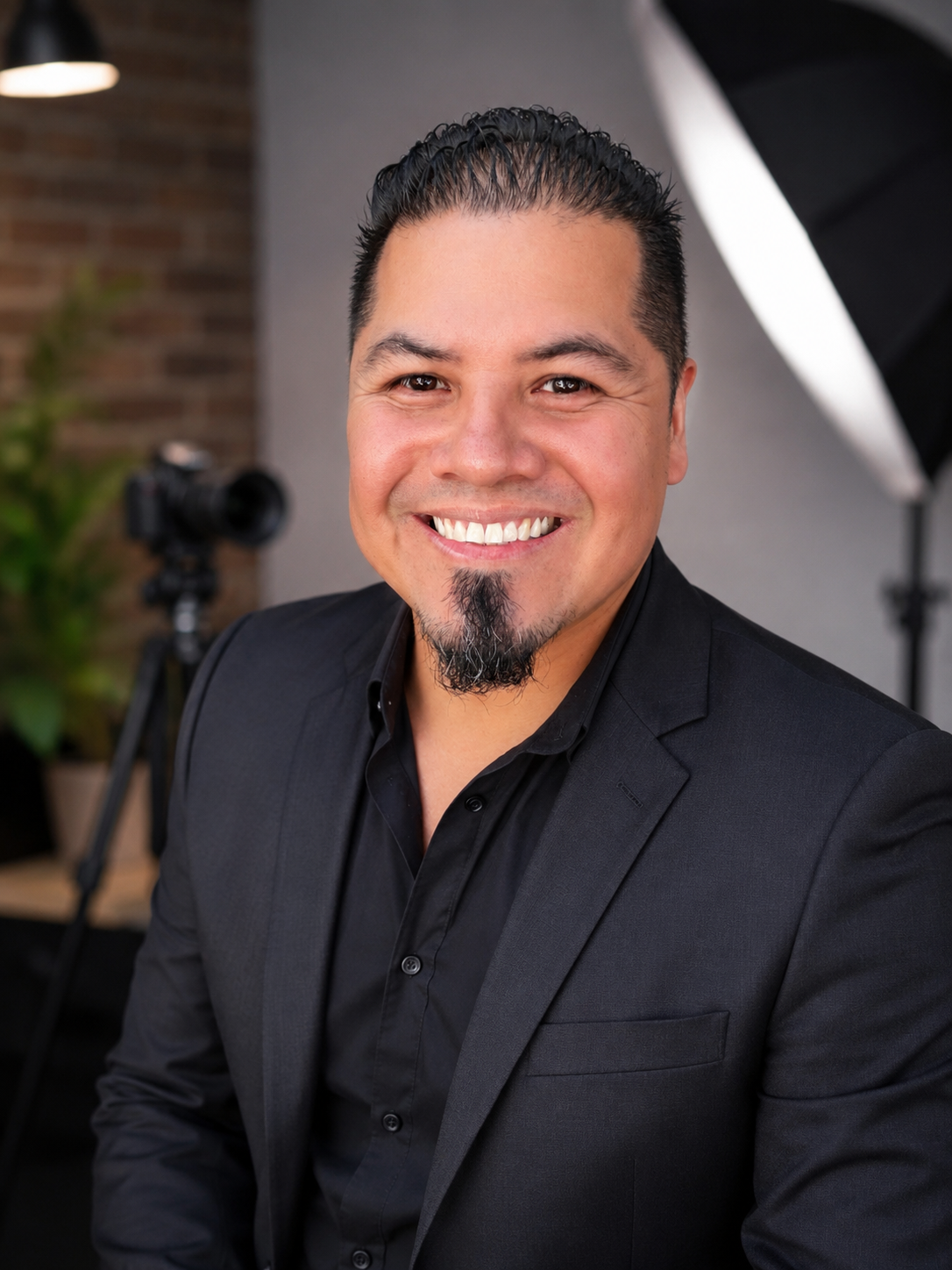 Carlos Quintero, founder of The Merchant Era, smiling in a black suit jacket and black shirt